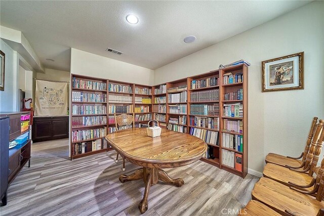 living area featuring light wood finished floors, bookshelves, and visible vents
