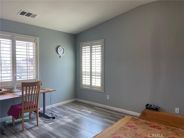 office featuring wood finished floors, vaulted ceiling, visible vents, and a healthy amount of sunlight