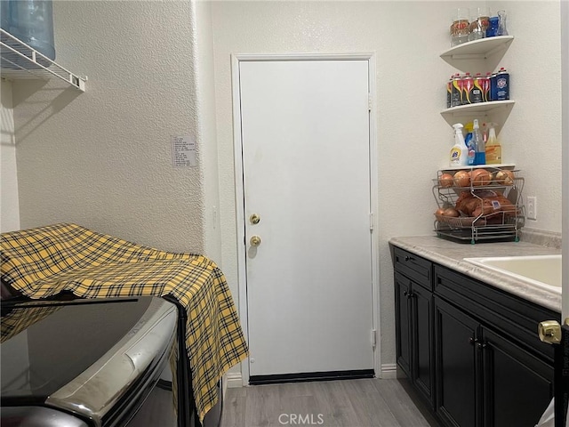 laundry area with light wood finished floors, a sink, and cabinet space