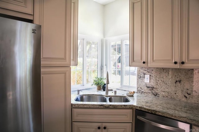 kitchen featuring cream cabinets, light stone countertops, stainless steel appliances, and a sink
