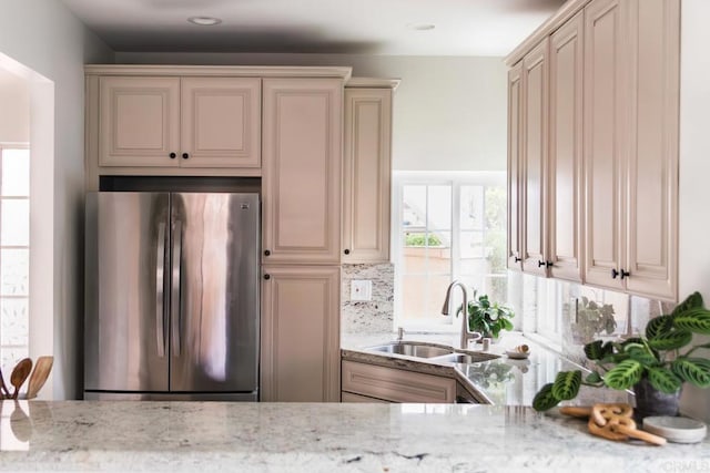 kitchen featuring a sink, cream cabinets, backsplash, light stone countertops, and freestanding refrigerator