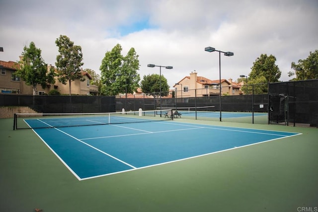 view of tennis court with community basketball court and fence