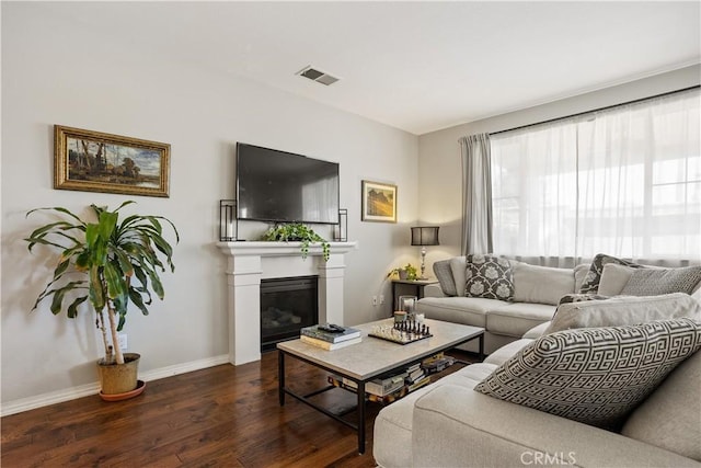 living room featuring dark wood finished floors, baseboards, a glass covered fireplace, and visible vents