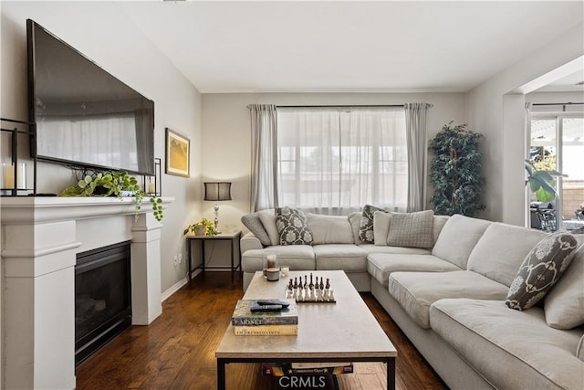 living area with baseboards, a glass covered fireplace, and dark wood-type flooring