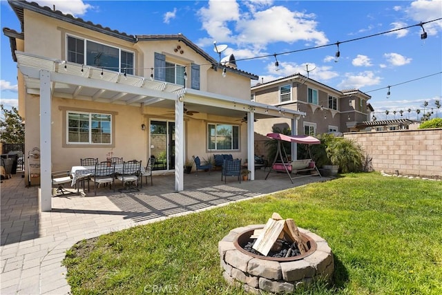 rear view of house with a ceiling fan, a yard, an outdoor living space with a fire pit, a patio, and stucco siding