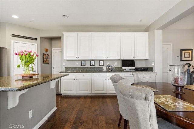 kitchen featuring dark stone countertops, a kitchen bar, white cabinetry, and dark wood-style flooring