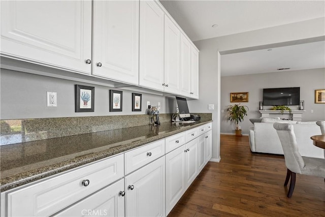 kitchen with dark stone counters, dark wood finished floors, open floor plan, baseboards, and white cabinetry