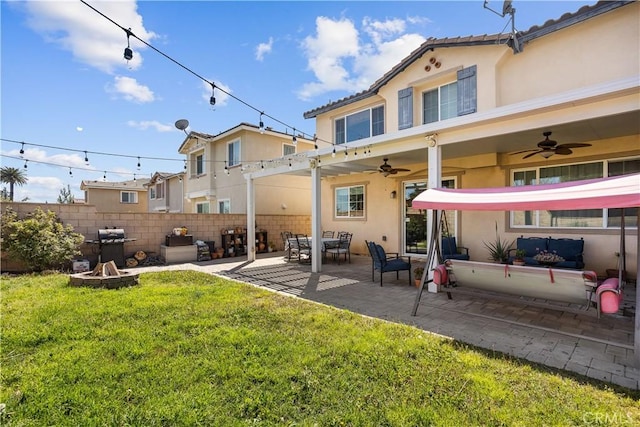 back of house with a ceiling fan, fence, stucco siding, a lawn, and a fire pit