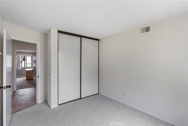 unfurnished bedroom with a textured ceiling, a closet, light carpet, baseboards, and visible vents