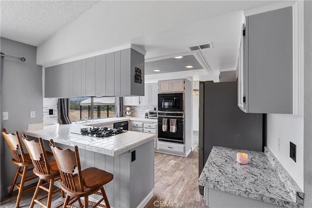 kitchen featuring a peninsula, light wood-type flooring, visible vents, black appliances, and a breakfast bar area
