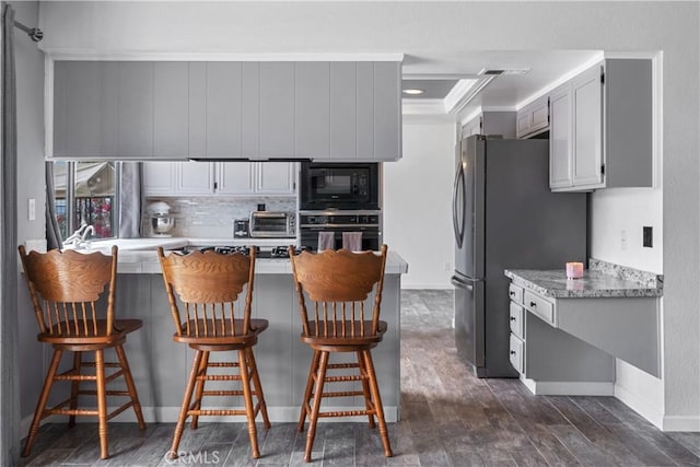 kitchen with visible vents, black appliances, tasteful backsplash, a breakfast bar area, and dark wood-style flooring