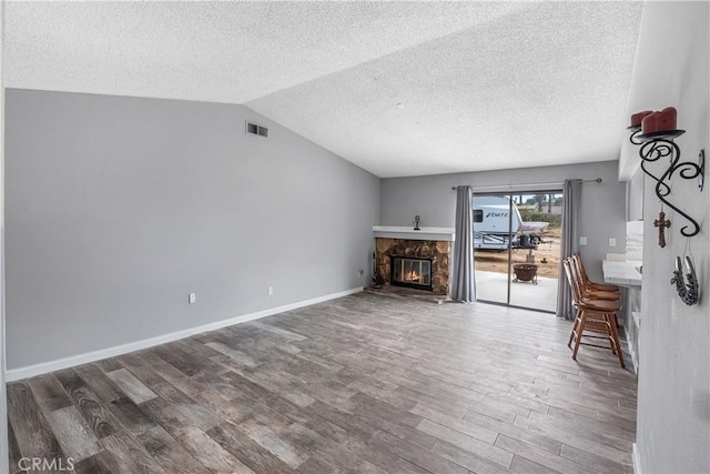 living room with a textured ceiling, vaulted ceiling, visible vents, wood finished floors, and a fireplace