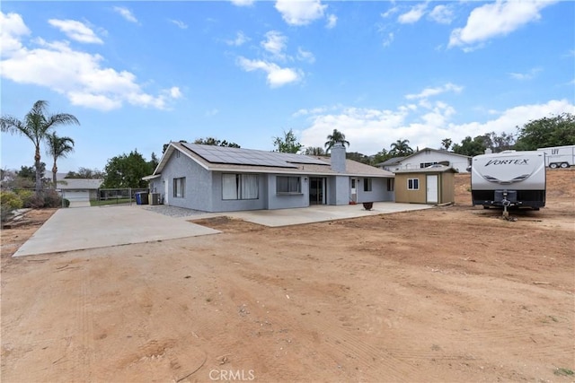 rear view of house with roof mounted solar panels, a patio area, dirt driveway, and a chimney
