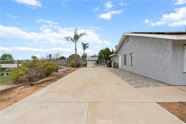view of property exterior with fence, driveway, central AC, and stucco siding