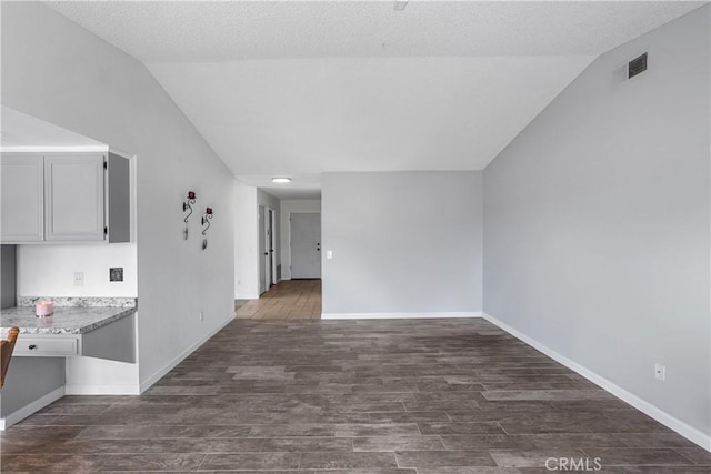 interior space with lofted ceiling, dark wood-type flooring, visible vents, and baseboards