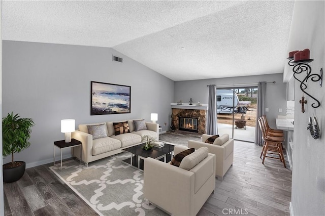 living area featuring vaulted ceiling, wood finished floors, visible vents, a stone fireplace, and a textured ceiling
