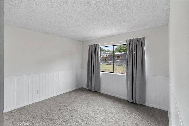 carpeted spare room with a wainscoted wall and a textured ceiling
