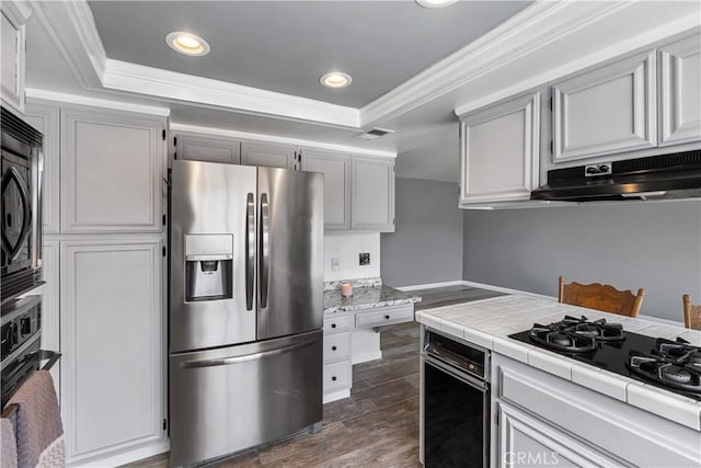 kitchen with under cabinet range hood, stainless steel fridge with ice dispenser, a raised ceiling, tile countertops, and gas cooktop