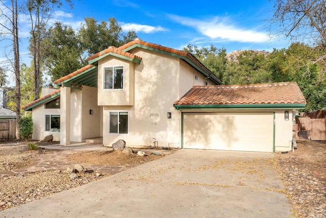 mediterranean / spanish house featuring fence, a tile roof, concrete driveway, and stucco siding