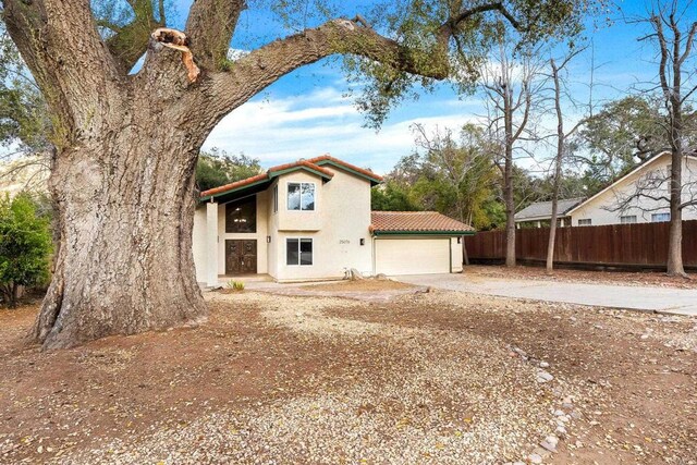 view of front of home with a tiled roof, driveway, fence, an attached garage, and stucco siding