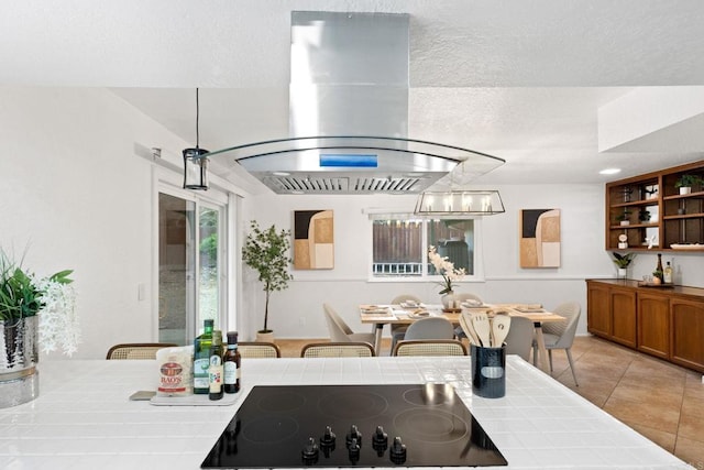 kitchen featuring open shelves, tile counters, a textured ceiling, island range hood, and black electric stovetop