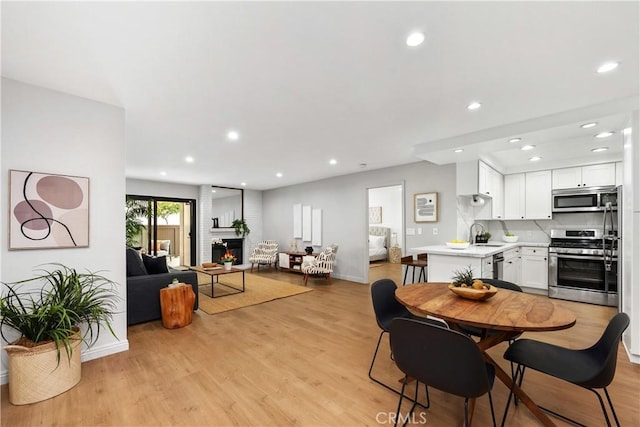 dining room with recessed lighting, light wood-style floors, a fireplace, and baseboards