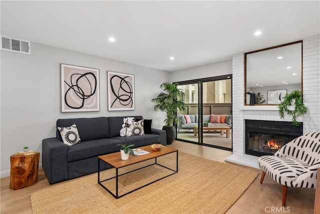 living room featuring wood finished floors, a brick fireplace, visible vents, and recessed lighting