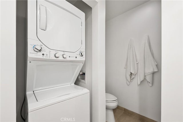bathroom with stacked washer and dryer, toilet, baseboards, and tile patterned floors