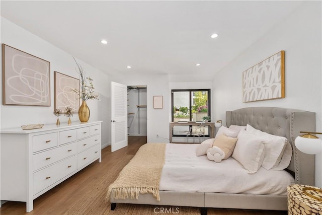 bedroom with recessed lighting, wood finished floors, and a walk in closet