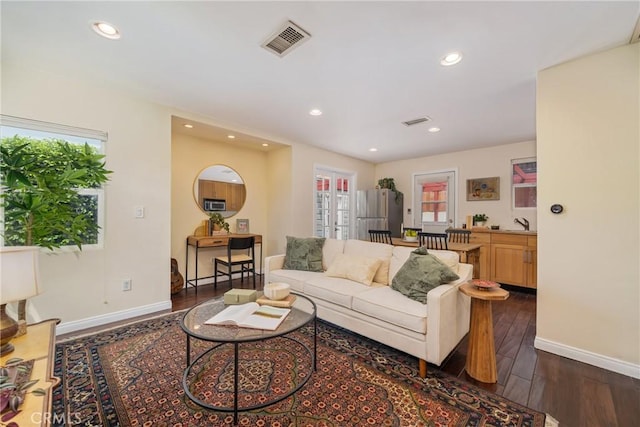 living room with baseboards, visible vents, a wealth of natural light, and dark wood-type flooring