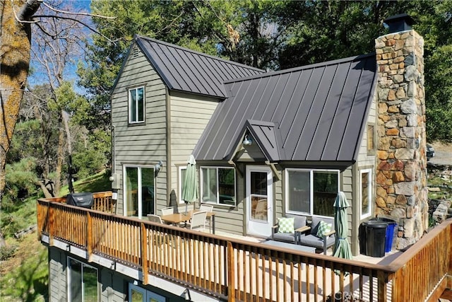 back of house featuring a chimney, a wooden deck, a standing seam roof, and metal roof