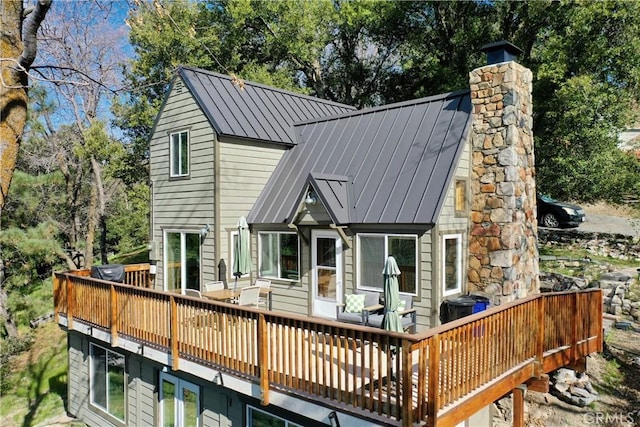 back of property with a wooden deck, a chimney, a standing seam roof, and metal roof