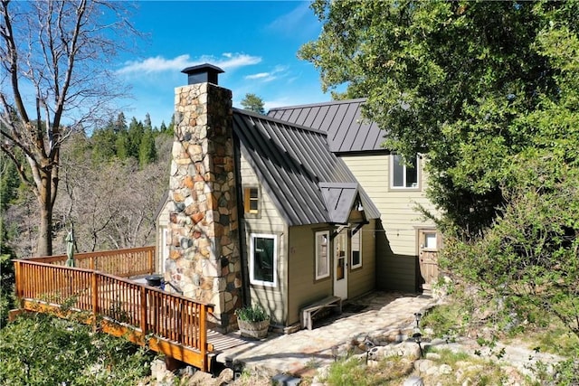rear view of property featuring a standing seam roof, a chimney, a wooden deck, and metal roof