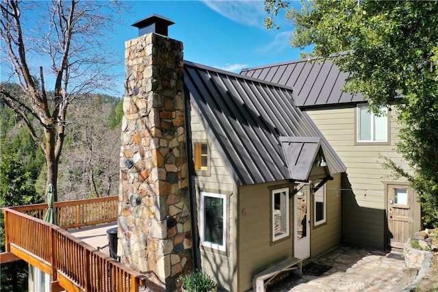 rear view of property with a standing seam roof, a chimney, a wooden deck, and metal roof