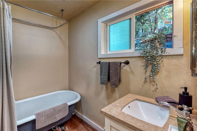 full bath with wood finished floors, baseboards, vanity, and a freestanding bath