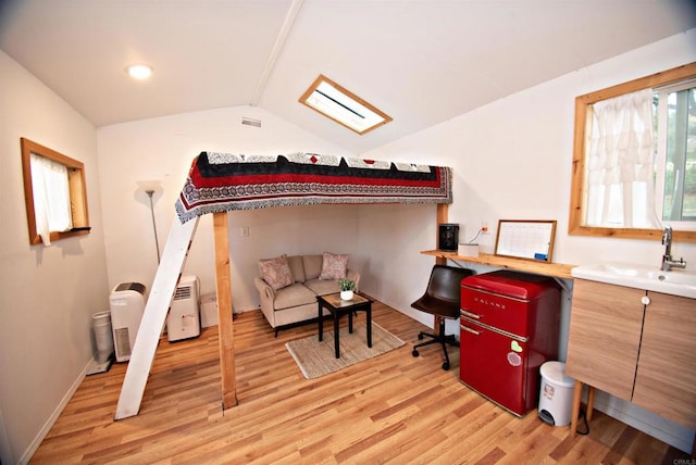 bedroom with light wood finished floors, vaulted ceiling, and a sink