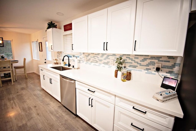 kitchen featuring stainless steel dishwasher, a sink, light wood finished floors, backsplash, and white cabinetry