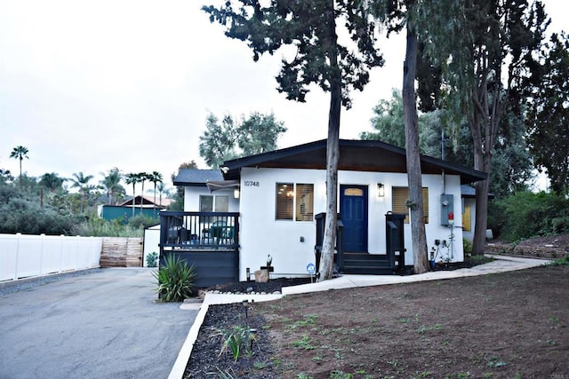 bungalow featuring a wooden deck, aphalt driveway, stucco siding, and fence