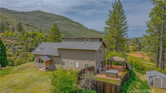 back of property with an outdoor structure, a storage unit, a gazebo, fence, and roof with shingles