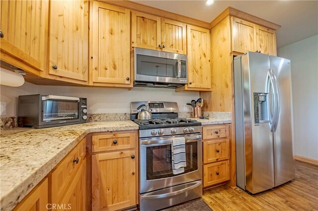 kitchen with appliances with stainless steel finishes, a toaster, light brown cabinetry, and light wood finished floors