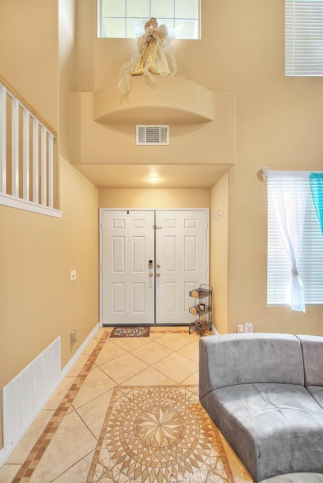 tiled entryway with baseboards, a towering ceiling, and visible vents