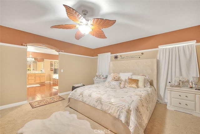 bedroom with ceiling fan, light carpet, ensuite bathroom, and baseboards