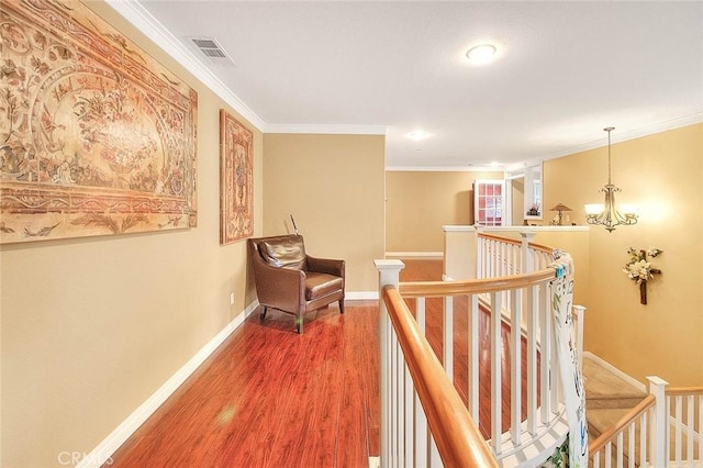 hallway with wood finished floors, visible vents, an upstairs landing, crown molding, and baseboards