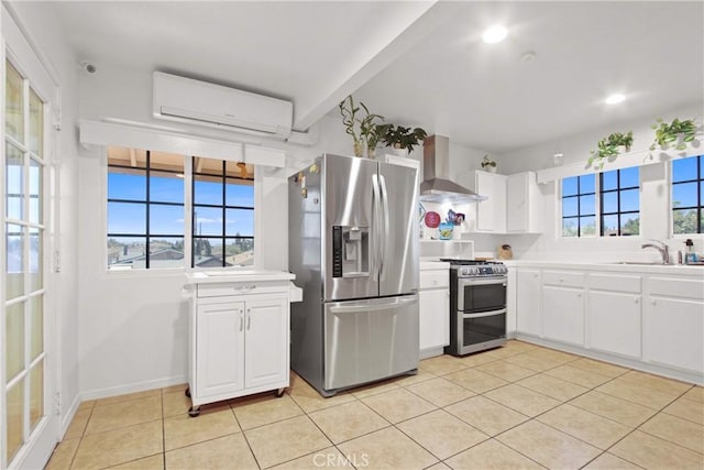 kitchen featuring a sink, a wall unit AC, light tile patterned flooring, wall chimney range hood, and appliances with stainless steel finishes