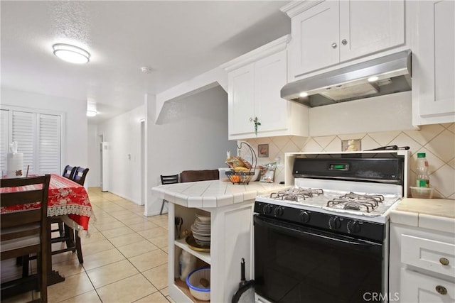 kitchen featuring gas range, white cabinets, under cabinet range hood, and tile counters