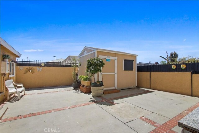 view of side of property with a patio area, a fenced backyard, an outdoor structure, and a shed