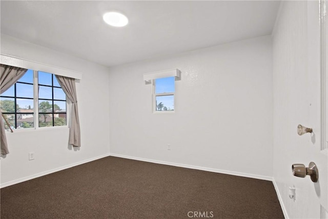 spare room featuring baseboards and dark carpet