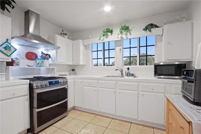 kitchen featuring stainless steel appliances, wall chimney range hood, tile countertops, light tile patterned floors, and a sink