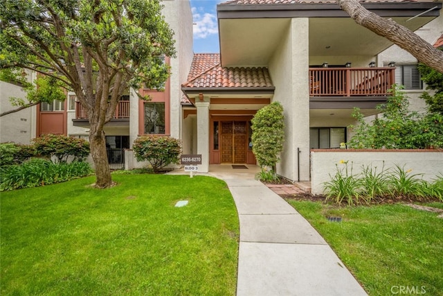 mediterranean / spanish home featuring a tile roof, a balcony, a front yard, and stucco siding