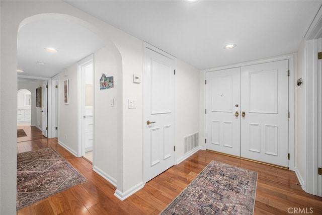 entryway featuring wood finished floors, arched walkways, baseboards, visible vents, and recessed lighting